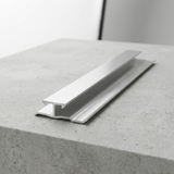 Brushed aluminum seamless trim connector displayed lengthwise on a concrete surface