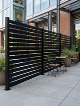 Dark aluminum open slat fence panels installed as a privacy divider around an urban patio seating area
