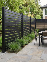 Dark aluminum open slat privacy fence surrounding a backyard dining patio with ornamental grasses